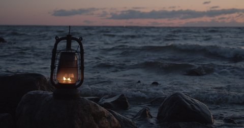 Oil lantern burning on rock in sea water at sunset