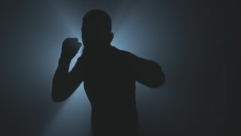 Male boxer punching to camera. Silhouette of young boxer practicing boxing punches looking at camera in dark smoky gym. Slow motion. Close-up in 4K, UHD