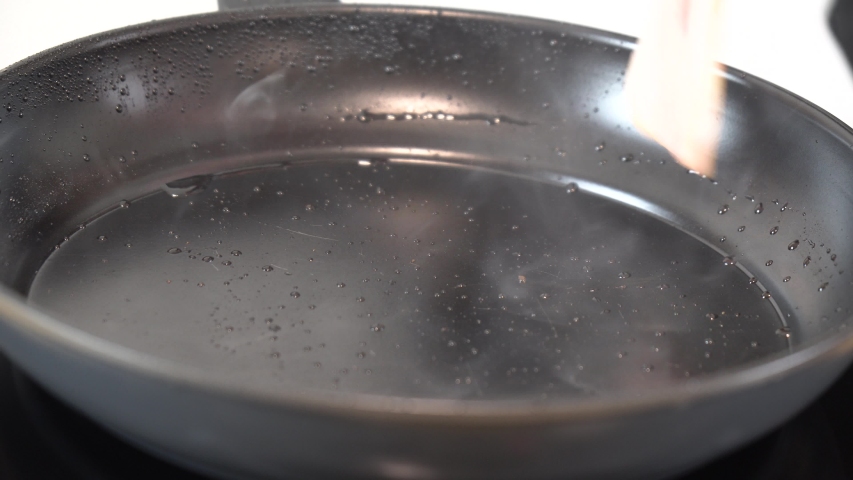 Young girl frying bacon on a black pan in the kitchen