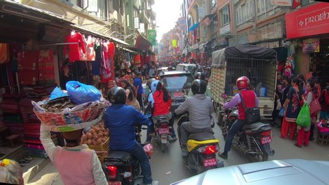 KATHMANDU, NEPAL - OCTOBER 24th, 2019. Typical colorful street scene in Kathmandu, Nepal, crowded by people, motorcycles and cars hard passing. Tourist area with shops selling gears and souvenirs