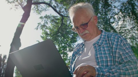 Old man in glasses trying to use computer in park