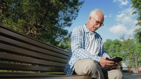 Old man with glasses and mustache is sitting on bench in park and reading ebook - Powered by Shutterstock - Get 15% off with code: PIKWIZARD15