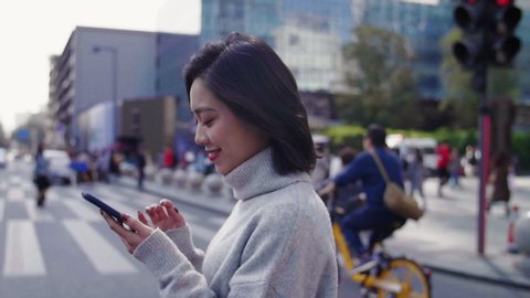 Slow motion Cheerful asian woman looking at mobile phone walking in the street to the office business urban people commuter with cellphone in hand 
