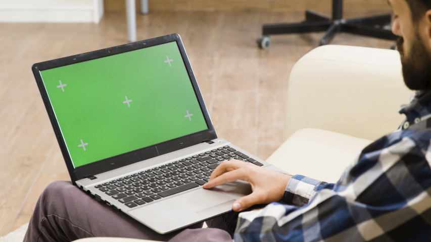 Man on the sofa looking at green screen laptop in a bright and well lit living space