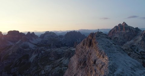 A cross on a mountain range in the Italian Alps / Dolomites. A beautiful view on the last minutes of a breathtaking sunset. Aerial view / drone flight.