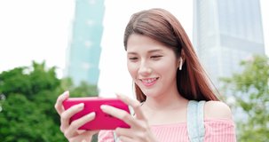 asian woman play mobile game with 5g smartphone outdoor - location taipei and taiwan