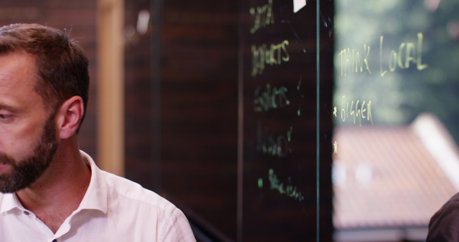 4K Businessman leading a brainstorming meeting, writing notes on glass screen