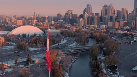 Aerial: Establishing shot of the Calgary city skyline and Canadian Flag flapping in the wind at sunrise. Calgary, Alberta, Canada. 
