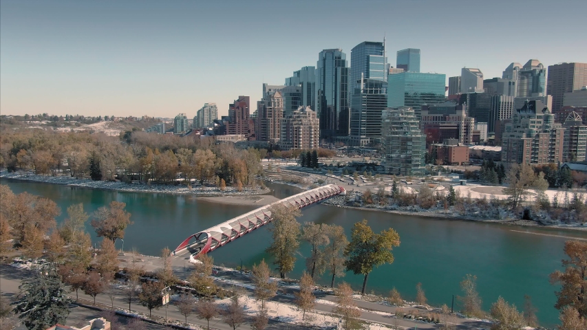 Aerial: Establishing shot of the Calgary city skyline. In the foreground is the Peace Bridge & the Bow River 