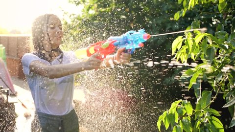 Slow motion closeup footage of wet teenage girl shooting water from toy gun during water fight at backyard