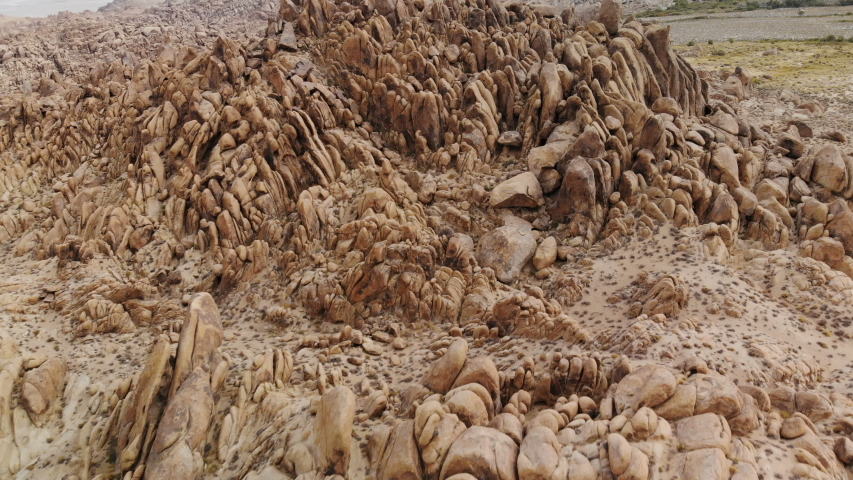 Aerial shot of rugged rocky terrain with alpine mountain backdrop at Alabama Hills in Eastern Sierra, California -Fly Over-