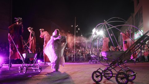 KAMENKA BUZKA, UKRAINE - SEPT 14, 2019: Performers hold baby, move carriages, smile. Stage in purple light. Female in white happy, moving closer to camera.