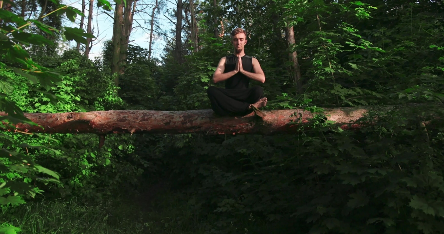 Bearded man sitting in pose of lotus with their eyes closed and meditating, orange kitten is sitting on his lap. Yoga outdoor concept.