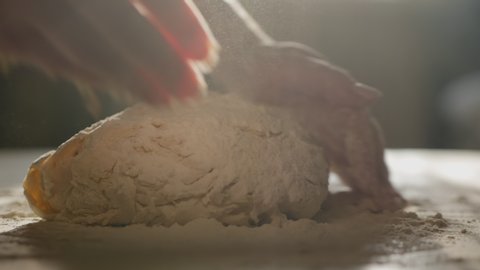 Female hands kneading dough in flour on the table, slow motion, sunlight from the window illuminates the scene.