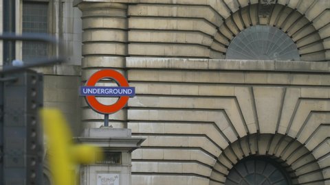 London, UK - April, 2019: Red Bus Drives Near London Underground Sign. London Underground sign near the entrance to the subway station. London Underground sign on the facade of a building in the city