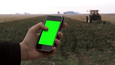 La Pampa province / Argentina - 09 09 2019: Male Hand Using An Old Smartphone With Green Screen In A Rural Field. A Tractor in the Background. 