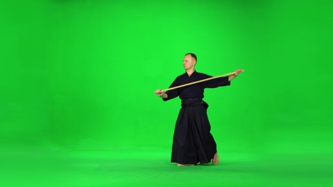 Masculine Kendo warrior practicing martial art with the bamboo bokken on green screen.