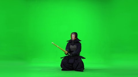 Masculine Kendo warrior practicing martial art with the bamboo bokken on green screen.
