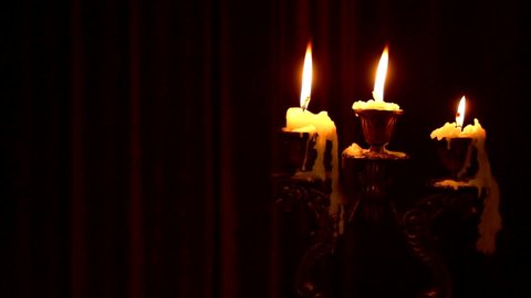 Three candles burn in a candlestick on a black background. Wax dripped from a burning candle. Gothic candlestick with candles. Dark gothic background
