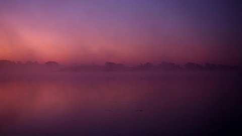Mist over the river. Dusk over the lake. Very dense fog. Dawn in morning. Red sky over the water. The morning comes. Forest reflected on water surface. Misty morning sky. Gothic background