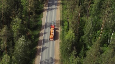 Gasoline tanker / orange fuel truck fast driving on straight freeway in countryside dense forest at summer sunny day / Aerial drone view