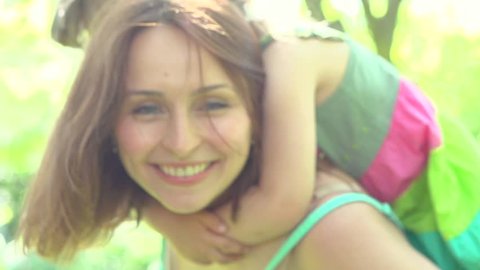 Mother and her little daughter having fun outdoors. Beautiful family mom and her child girl hugging and kissing together. Piggyback. Happy parent and baby. Slow motion 240 fps, high speed camera 1080p