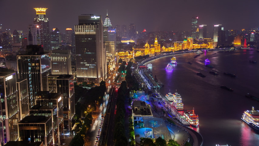 Timelapse famous Waitan with Shanghai motorboats at piers and sailing along wide calm Huangpu river reflecting city lights at night in China