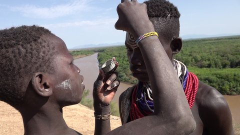 OMO VALLEY, ETHIOPIA – MARCH 2019: Young tribal men decorate their faces with paint in preparation of tour group in Kolcho village in the Omo Valley in South Ethiopia