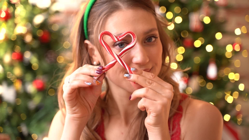 new year portrait of a woman smiling and holding a heart in the hands of sweet sticks of caramel in the form of a cane. girl with Christmas mood, beautiful outfit