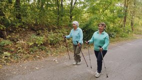 Elderly senior women practicing Nordic walking outdoors, healthy lifestyles in old age. Women walk along the road. Slow-motion 4k video