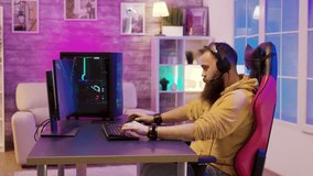 Man sitting on a gaming chair and playing video games in his room with colorful neons wearing headphones.