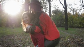 friendly relations, happy young woman jumps over her female friend back and enjoying a piggyback on sunny day in autumn park