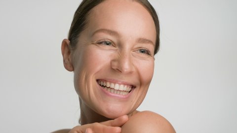 Close-up beauty portrait of young woman with smooth healthy skin, she gently touches her shoulders with her fingers on white background and smiles