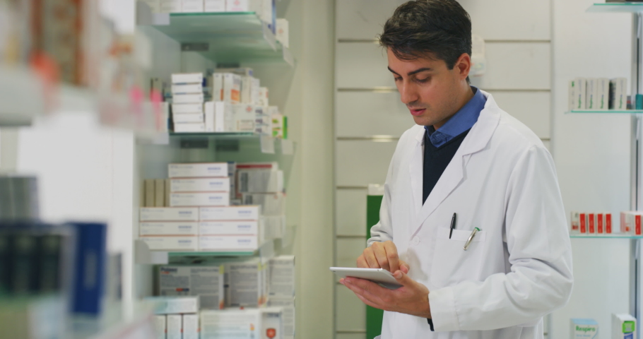 An young male pharmacist consultant is checking with a tablet medicines on the shelf of drug store.  | Shutterstock HD Video #1041405601