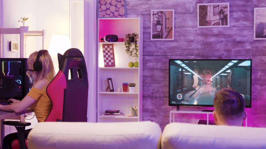 Man losing at professional online shooter game in a room with colorful neon lights. Girl playing online games sitting on gaming chair