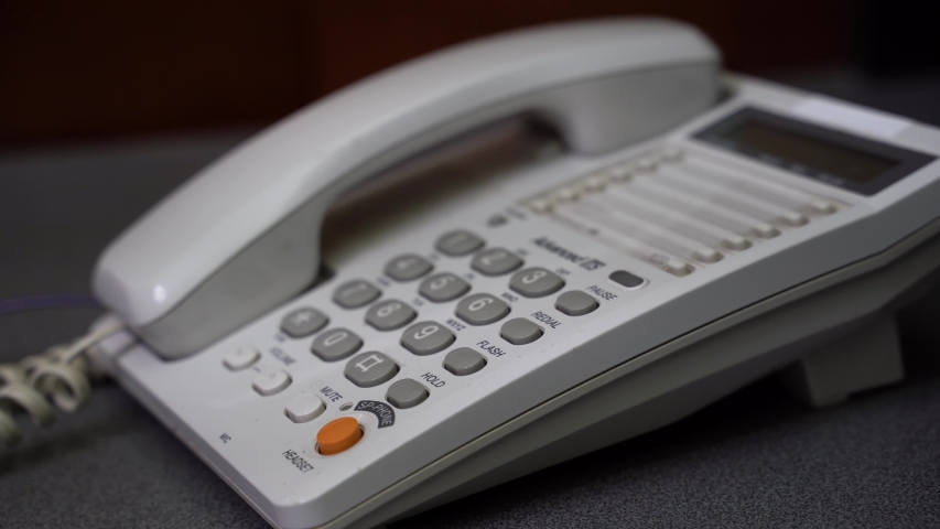4K Men's Hand Dials On The Number Buttons On The A Wired Phone. Low angle closeup view of male hand picking up handset and dialing telephone number on white landline phone keypad. Royalty-Free Stock Footage #1041428371