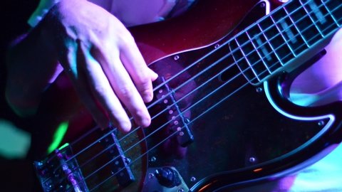 Man playing bass guitar with band on concert, close up. Young musician playing a electric bass guitar on stage. Bass guitar player playing with his fingers and hands on festival. Music instrument
