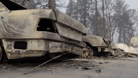 Burned cars in Paradise, CA after the Camp Fire. Melted plastic on ground, destroyed trees and smoke in background.