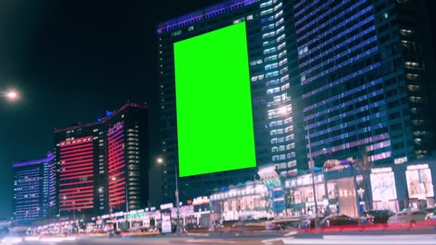 Large billboard with green screen for advertising on the modern building with neon lights, blank billboard opposite the road, timelapse of traffic on busy highway, cyberpunk colors