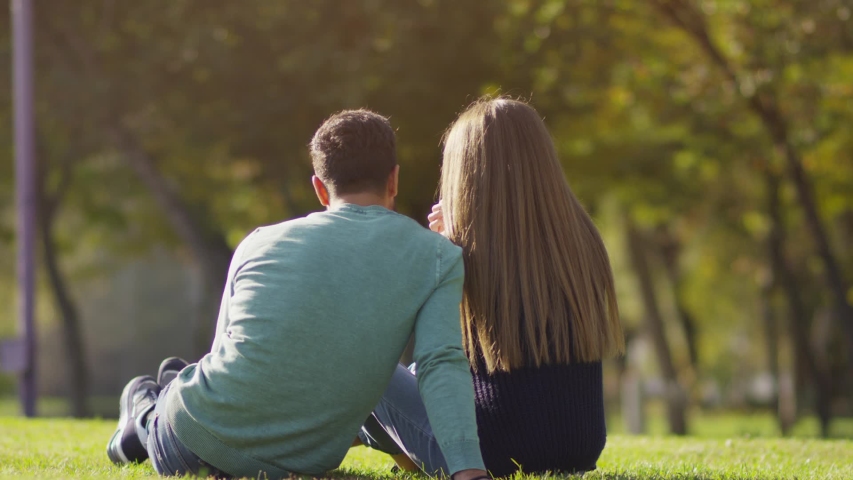 Back view of happy lovely caucasian romantic couple sitting on lawn and hugging each other in park . Rear view of young couple sit on grass and enjoy in the open air. Happiness people . Slow Motion . | Shutterstock HD Video #1041446443