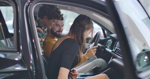 Side view of happy Caucasian wife sitting in car salon with family and discussing purchase. Young businesswoman choosing new car with husband and son. Car business. Cinema 4k footage ProRes HQ.
