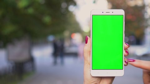 Close up hands woman holding use white phone with green screen on busy street background scrolling pages swiping surfing internet technology smartphone chroma key message