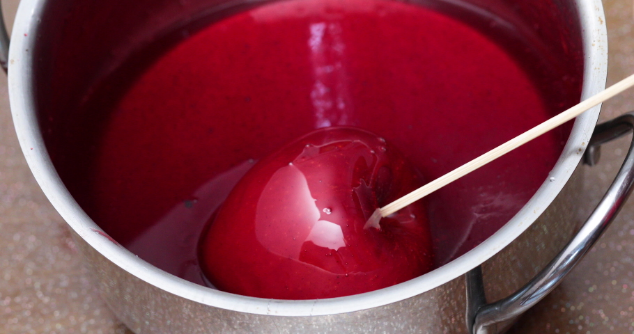 Hand holding apple by its stick dipping in syrup and turn to coat evenly - Preparation of candy apples