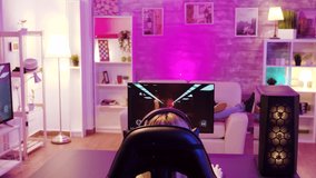 Over shoulder view of girl playing online shooter games sitting on gaming chair. Man with vr goggles in the background.