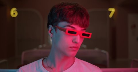 Portrait of Cool Millenial Guy Wearing Party Trendy Glasses Turning Head and Looking Straight to Camera with Futuristic Neon Lighting Numbers at the Background. Close Up shot.