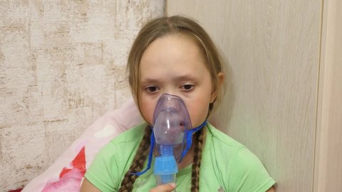 child with a tablet is sick and breathes through an inhaler. close-up. little girl treated with an inhalation mask on her face in hospital. Toddler treats flu by inhaling inhalation vapor.