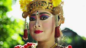 Bali female in sunlight wearing a traditional colorful jewelled costume performing in the art of dance and artistic facial expressions Indonesia Southeast Asia travel and tourism RED MONSTRO