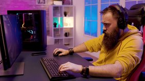 Hipster bearded man playing professional online games on his computer. Gamer in a room with colorful neon lights.