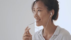 Positive happy asian business woman having a phone call using her wired headphones in the white office