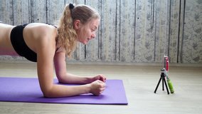 Young athlete doing plank exercise on gym Mat. Girl blogger in morning doing sports, looking at the camera and is live on your smartphone. The concept of a healthy lifestyle through online broadcasts